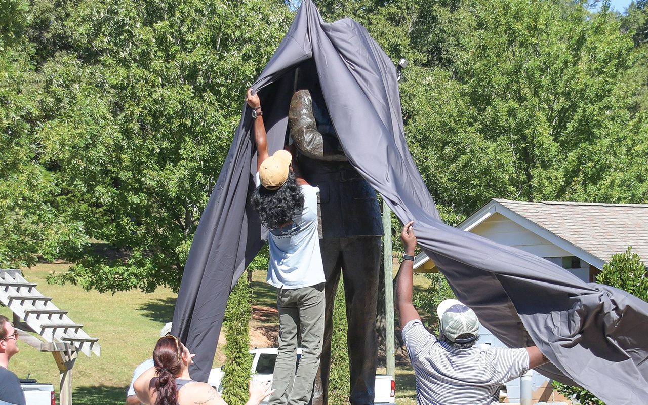 Nikki Barker (left) of the Eatonton Veterans Thrift Store, helps workers temporarily cover up the statue of Hiram Little.