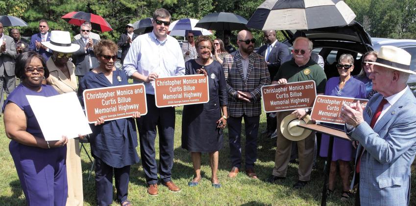 Ocmulgee Judicial Circuit District Attorney T. Wright Barksdale (4th from left, holding sign), Putnam County Sheriff Howard Sills (in green), and State Senator Rick Williams (far right), joined family members of Sgts. Monica and Billue as they received official sign replicas similar to those posted alongside Hwy. 16 in Putnam County. IAN TOCHER/Staff
