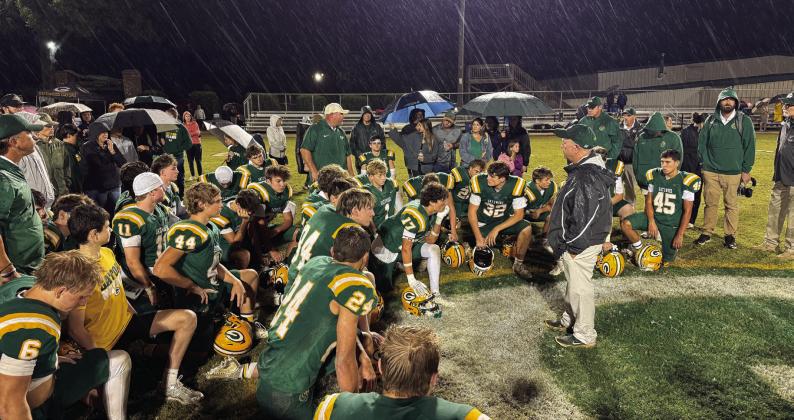 With steady rain falling, Gatewood head coach Jeff Ratliff (right, black jacket) addresses his team at midfield after a disappointing 30-17 loss last Friday to the visiting Windsor Academy Knights, from Macon.