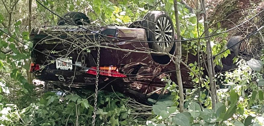 A chain hangs from the overturned Nissan as Hurt’s Towing prepares to remove it from the woods at the end of East Sumter Street Monday. LYNN HOBBS/Staff
