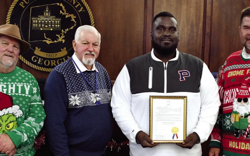On behalf of his fellow coaches and a roster 39 players, Alexander Banks, head coach of the 2025 Putnam County Middle School War Eagles football team, accepted a framed proclamation last Tuesday night recognizing the team’s 2025 state championship from (l-r) Commissioner Jeff Wooten, Chairman Bill Sharp, and Commissioner Tom McElhenney. IAN TOCHER/Staff