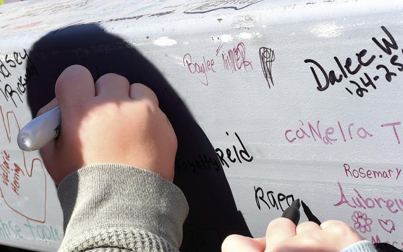Current students add their names to an already well-covered structural beam destined for use in the new Putnam County Elementary School. IAN TOCHER/Staff