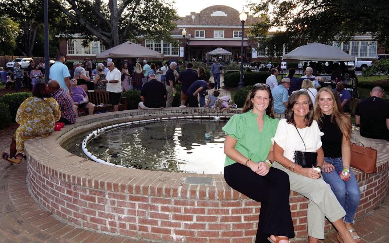 Linda Moore (center) with her daughters Abbey Kay Moore (left) and Autumn Askew sat on the fountain wall in front of The Plaza Arts Center while a band entertained the Taste of Eatonton crowd from the facility’s front steps (center, background). LEIGH LOFGREN/Staff