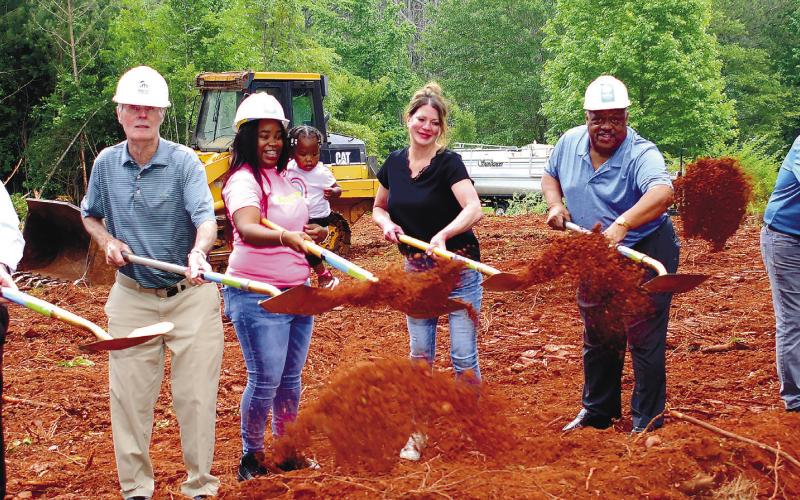 Throwing the first shovelfuls of dirt were (l-r): Bill Gower of Farmers and Merchants Bank, Habitat for Humanity’s Bucky Kahl, soon-to-be homeowner Camille Hyman with baby Carmoni, Habitat’s Jennifer Ishee, Eatonton Mayor John Reed and electrician Clay Lloyd. Hyman’s parents’ home is shown on the right. IAN TOCHER/Staff