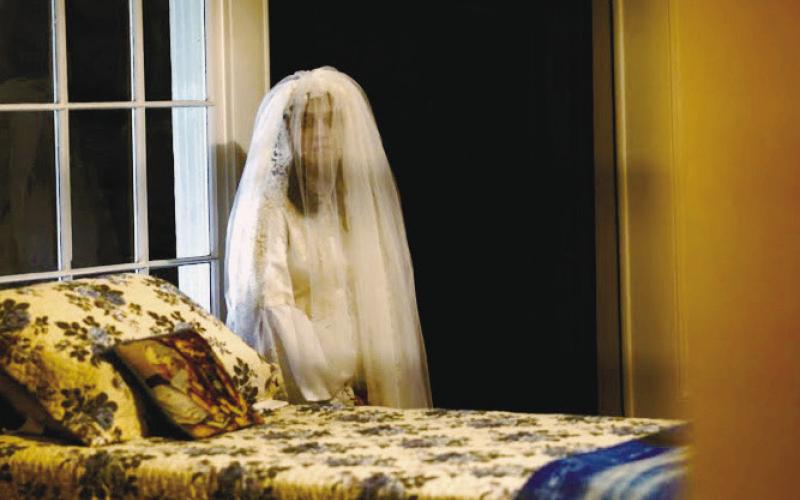 The actress playing Sylvia stands by the bedroom window on the second floor of Panola Hall, dressed in her trademark white wedding gown. GENE GARCIA/Contributed