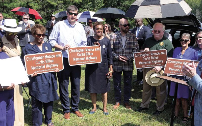 Ocmulgee Judicial Circuit District Attorney T. Wright Barksdale (4th from left, holding sign), Putnam County Sheriff Howard Sills (in green), and State Senator Rick Williams (far right), joined family members of Sgts. Monica and Billue as they received official sign replicas similar to those posted alongside Hwy. 16 in Putnam County. IAN TOCHER/Staff
