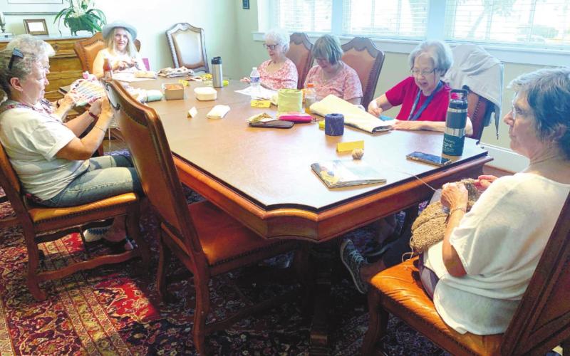 Seven members of Stitches and Stories work on their projects around The Plaza conference table. BAILEY BALLARD/Staff