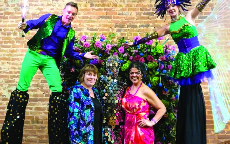 Sara Tomson-Hooper and Myrna Taylor pose under the floral frame with performers from Gravity Entertainment.