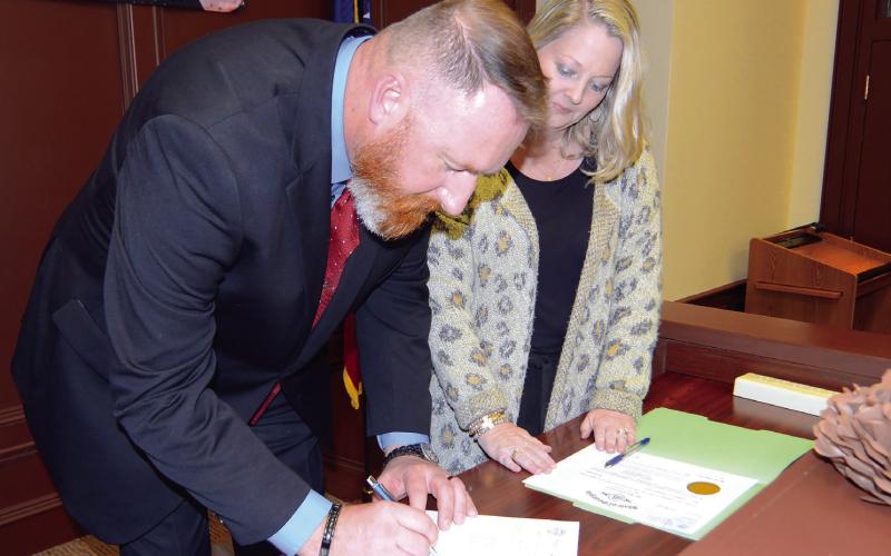 With Probate Court Judge Brandi T. Huskins by his side, Terrell Abernathy signs in for the first time as Putnam County’s newly installed Tax Commissioner. IAN TOCHER/Staff