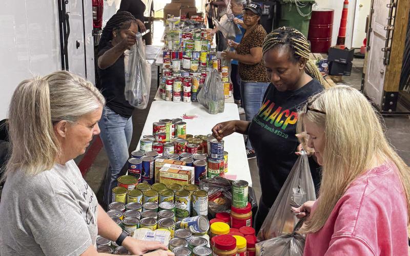 Kim Smith of the Eatonton Service League (foreground, left) joined several volunteers Friday morning in a storage area behind the Eatonton Fire Department garage to help prepare hundreds of bags of food for distribution Saturday morning. IAN TOCHER/Staff