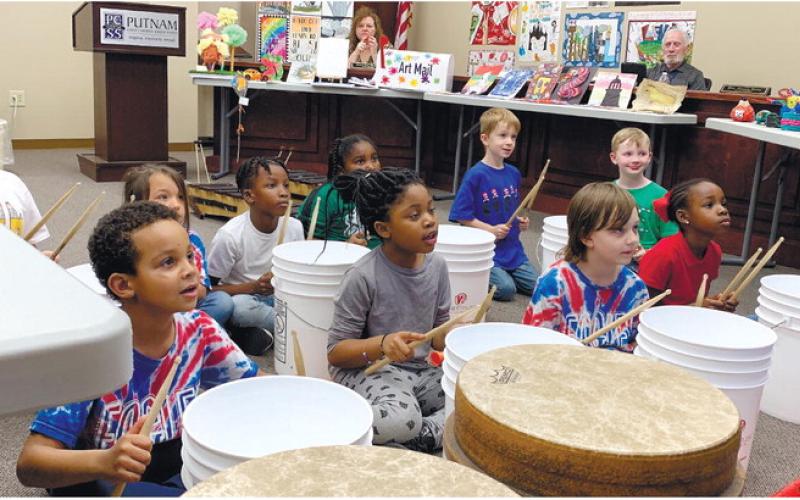 First and second graders perform the rhythm to the Mario theme as the board watches from behind in their seats.