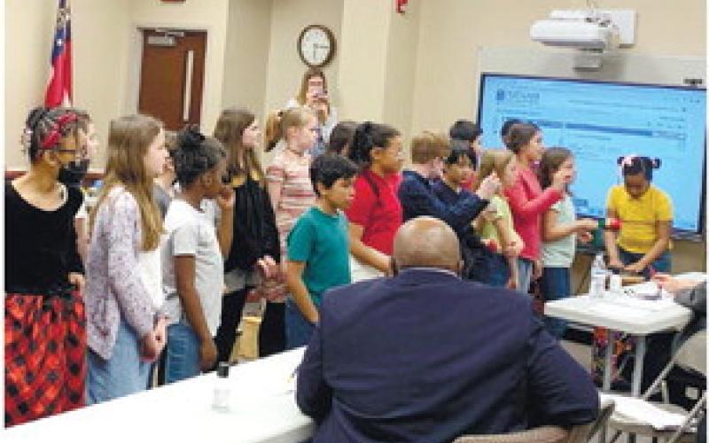 Third graders play xylophones as fourth and fifth grade prepare for to sing. Fourth and fifth graders sing two songs for the board while facing a large audience of parents and staff.