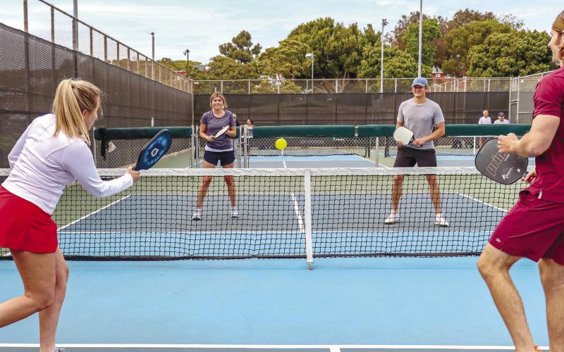 Dedicated pickleball courts appear like mini tennis courts, while the rackets look like oversized ping-pong paddles. The ball itself is plastic with holes throughout, similar to what’s commonly known as a whiffle ball. Mixed doubles (shown) is a very popular team option for the socially oriented sport. CONTRIBUTED