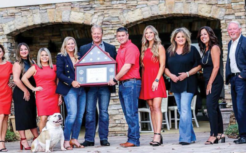 Members of the Kim and Lin Logan Team display a flag once flown over Camp Arifjan in Kuwait, presented to them by U.S. Army National Guard Major Brett Thomas in recognition of their support of “citizen soldiers” abroad.
