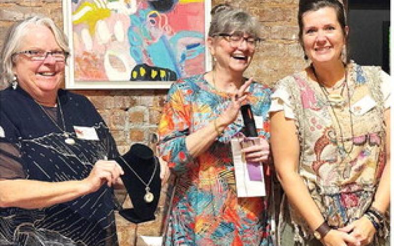 L-R: Art show chairperson Michele Hartung and co-chair Cathy McIntire congratulate The Artisans Village communications specialist Melanie Schneider after she won a Merit Award for “Golden Spiral,” a necklace she designed and created. IAN TOCHER/Staff