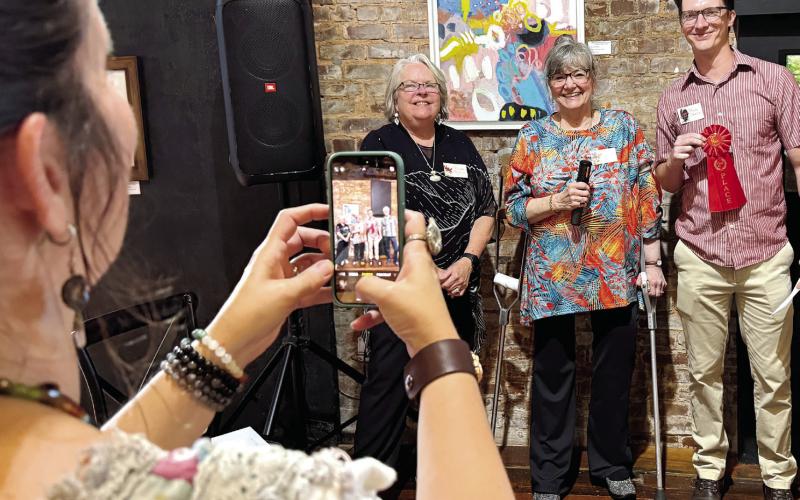Melanie Schneider of The Artisans Village takes a cellphone pic of second-place winner Brian Danson for “Stand Strawng!” a welded sculpture of a bulldog he entered in the 9th annual Lake Country Juried Art Show. IAN TOCHER/Staff