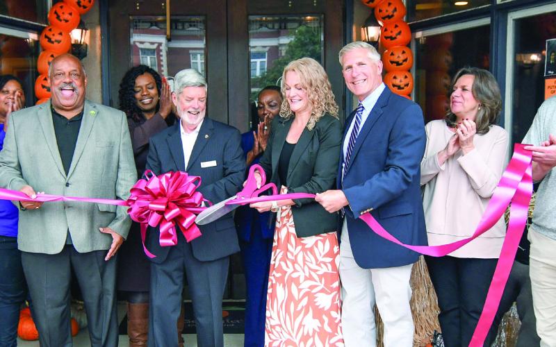 Eatonton-Putnam Chamber of Commerce President Robbie King (center with bow) watches as Courtney Adkinson cuts the ribbon with her husband Frank at her side, to officially announce the opening of Luxury Outdoor Travel, near Publix in Greene County. IAN TOCHER/Staff