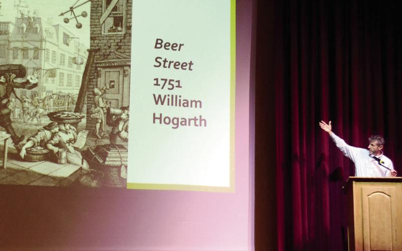 GCSU’s Dr. Eric Tenbus gestures toward the “Beer Street” political cartoon of artist William Hogarth during his talk at The Plaza Arts Center on Sunday afternoon. IAN TOCHER/Staff
