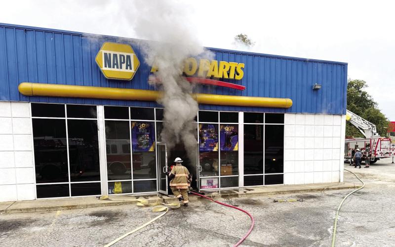 A City of Eatonton firefighter approaches the front door of the NAPA Auto Parts store on South Oak Street early Tuesday morning as Putnam County firefighters prepare their ladder truck in the side parking lot. COURTESY OF EATONTON FIRE DEPARTMENT