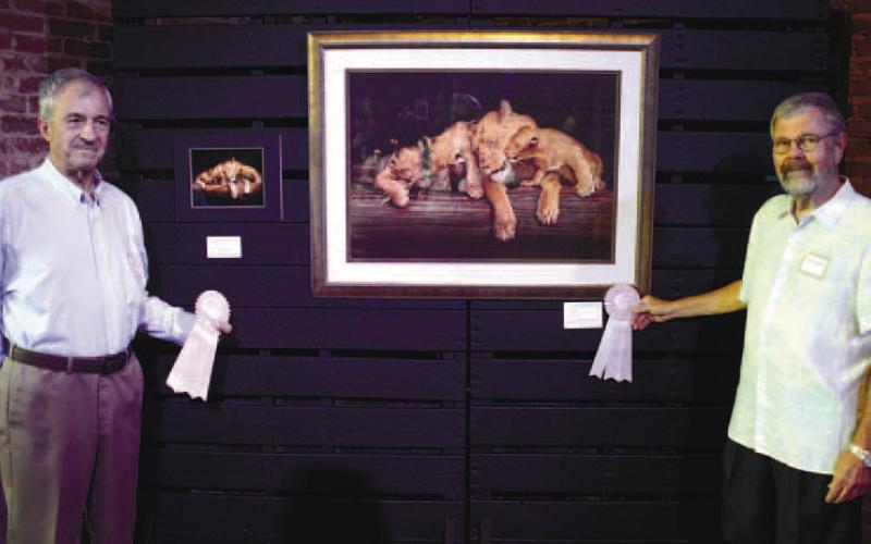 Greg Miller (left) stands alongside his photograph “Pride,” of a mother lion and her cubs, which served as the inspiration for artist Steve Kippels and his painting “Miller’s Cats.” Both pieces were voted People’s Choice by attendees Sept. 15, at the opening reception for this year’s Dual Vision: Art Through Different Eyes exhibition. IAN TOCHER/Staff