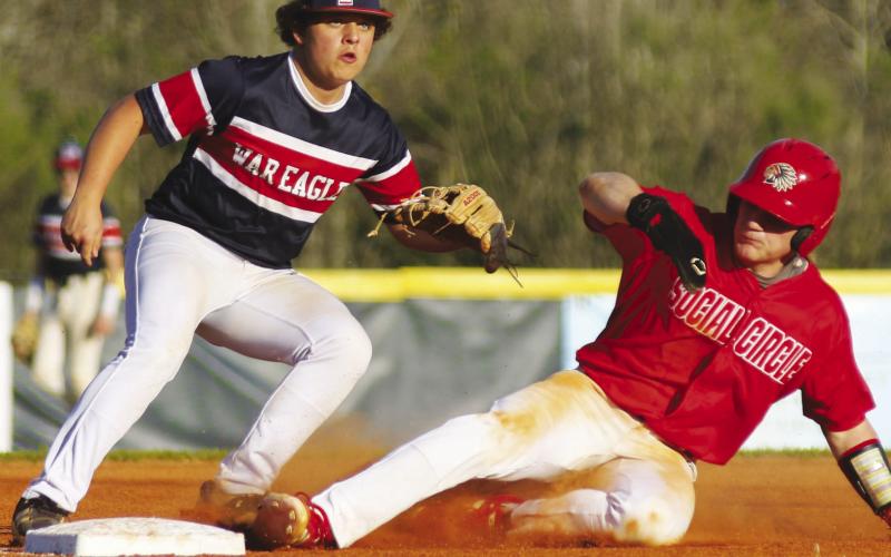 Putnam County junior Jackson Dodd (left) waits on a throw from the catcher as a Social Circle player (right) slides into third base safely. TREY NORRIS/Staff
