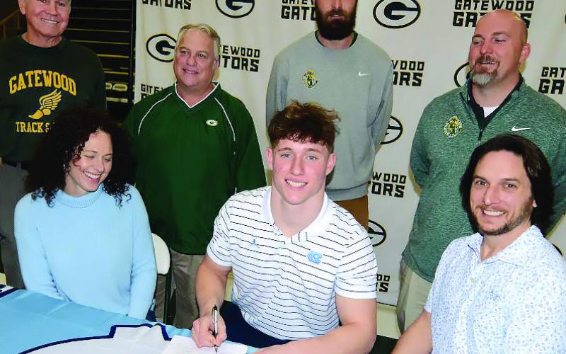 Sitting between his parents and backed up by football coaches (l-r) Mike Kelly, Jeff Ratliff, Josh Ringer, and Tyler VanDusen, Evan Bennett was all smiles as he faces a bright future with UNC. IAN TOCHER/Staff