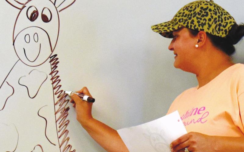 Teacher Anna Watkins demonstrates to the students how to draw a giraffe on the white board.
