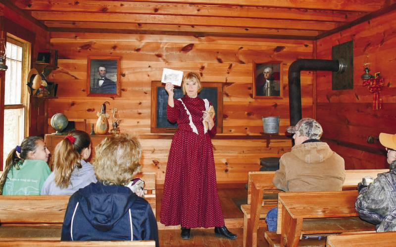 Lynn Romine tells the public what schools were like a hundred years ago. In her hands, she holds a picture of Rockville School, the first rural vocational school in Georgia, and still an existing building in Putnam County.