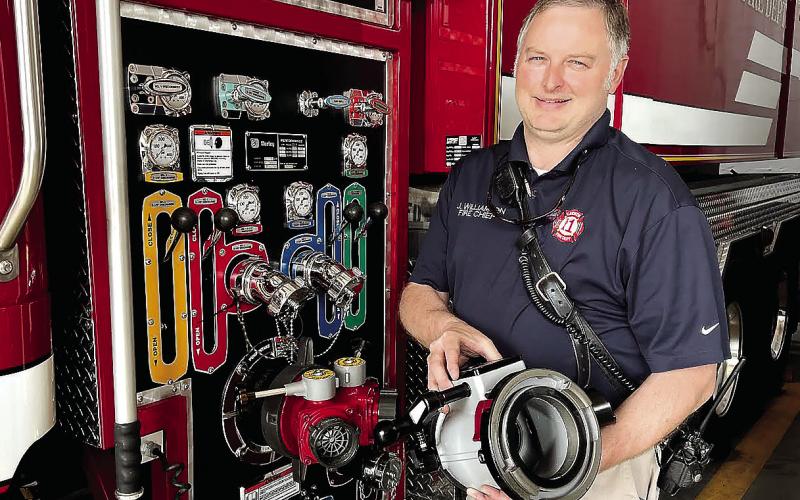 Eatonton Fire Department Chief Jamey Williamson holds one of the new 5-inch hose fittings he’s already received to replace the current 3-inch fittings (red fixture by his right hip). Now, he’s just awaiting delivery of new 5-inch fire hoses to install everything on the department’s trucks. IAN TOCHER/Staff