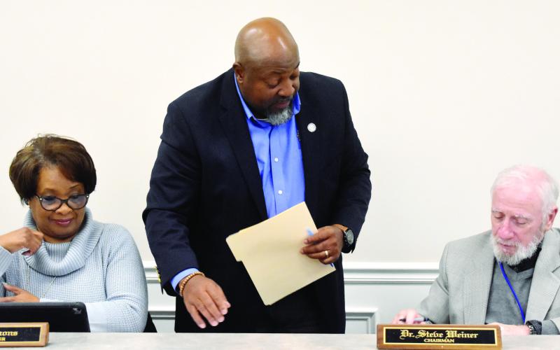 Austin (center) leans over Board Chair Dr. Steve Weiner’s shoulder as board members sign the approved contract. BAILEY McCULLY/Staff
