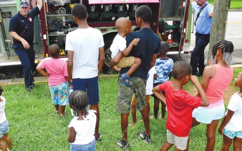 Eatonton firefighters Tim Epps (left) and Matt Kitchens explain the features of their firetruck to an interested crowd of local children. IAN TOCHER/Staff