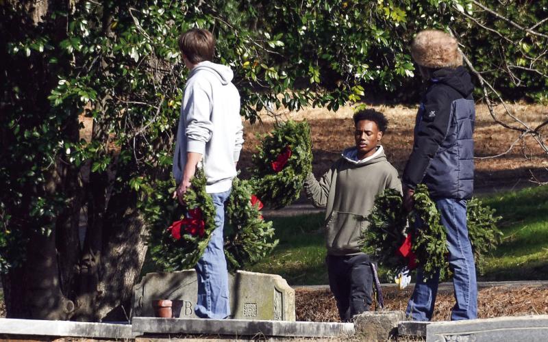 Three young friends have their hands full while placing wreaths as part of the Wreaths Across America program at Pine Grove Cemetery. IAN TOCHER/Staff