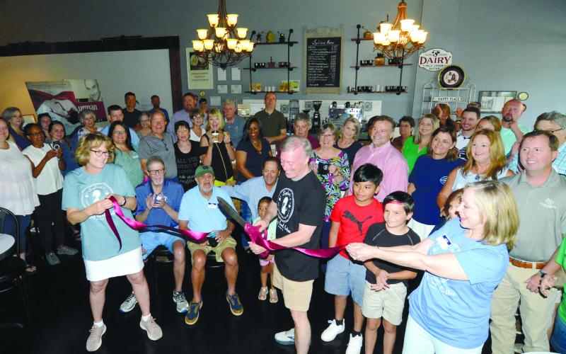 Shop co-owner Diana Homeier (left) and Paula Benjamin of the adjoining Georgia Writers Museum each held an end of the ceremonial red ribbon as Michael Homeier made the grand-opening cut last Friday to officially open Sylvia’s: A Supernatural Coffee Bar. IAN TOCHER/Staff