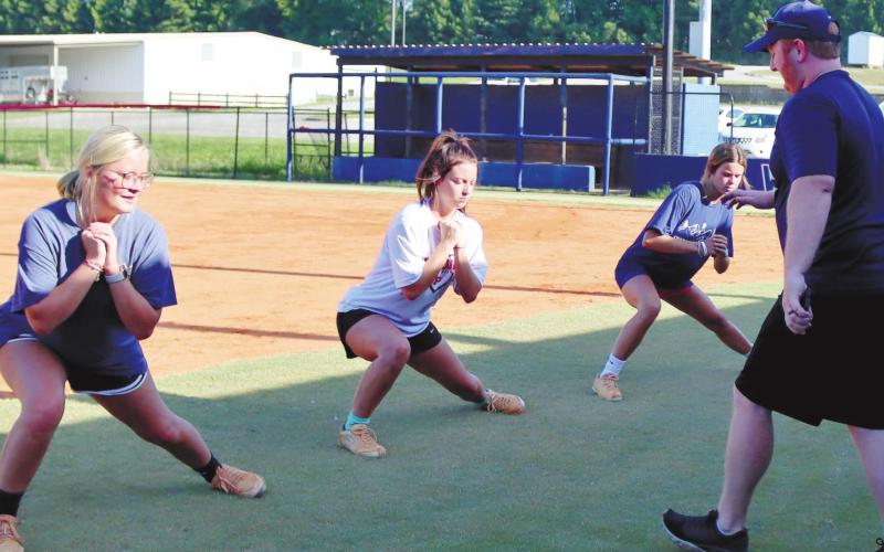 From left, Senior Jada McDerment Senior Sara Hulsey and Junior `Lily Frisch are led in a pitching exercise by Coach McElroy during summer workouts last week.