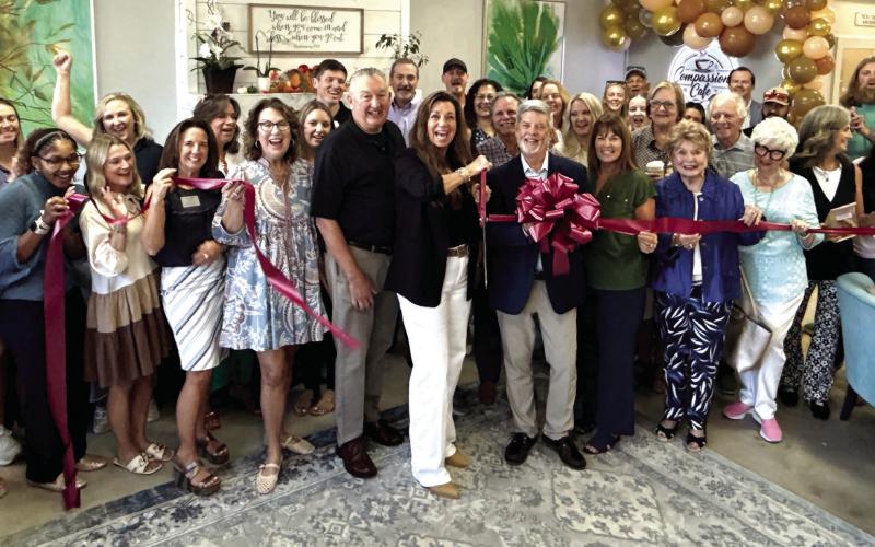 With husband Steve at her back, Compassion Café owner Lisa Tubbs wields the scissors for a ribbon-cutting ceremony arranged by Robbie King (behind bow) of the Eatonton-Putnam Chamber of Commerce. IAN TOCHER/Staff