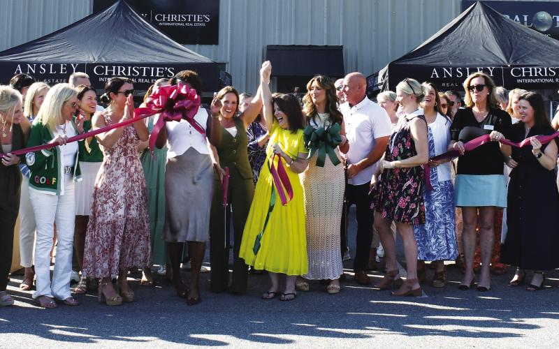 Adriana Velez (center with scissors) was joined by a large throng of business colleagues and well wishers last Thursday as she officially cut the ribbon to her new Ansley R.E.Christie’s Int’l. business center in a joint ceremony co-hosted by Eatonton-Putnam Chamber of Commerce President Robbie King and Greene County Chamber of Commerce President Mika Mills (both, far right). IAN TOCHER/Staff