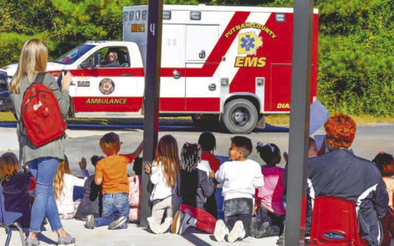 Children are waving and greeting the first responder and community service vehicles as they go by.