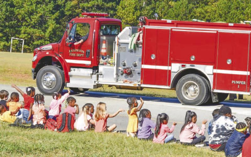 Children are waving and greeting the first responder and community service vehicles as they go by.
