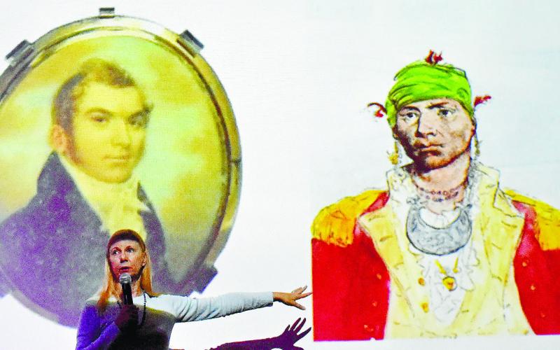 Mauriel Joslyn stands in front of the slide showing two portraits of Alexander McGillivray, the one on the right being a sketch by John Trumbull depicting him as an Indian Chief.
