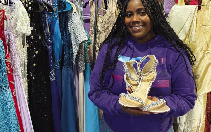 Reasha Daniels of Pretty Girlz Fitness in downtown Eatonton poses with just a few of the more than 200 formal dresses donated to provide local girls with prom and pageant gowns. IAN TOCHER/Staff