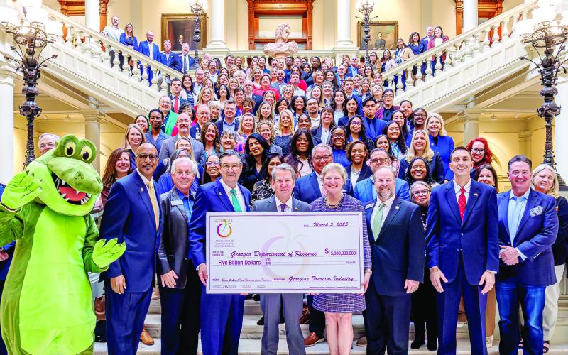 Gov. Brian Kemp (front center) accepts a symbolic $5 billion check from Amanda Dyson-Thornton, executive director of the Georgia Association of Convention &amp;amp; Visitors Bureaus. MMCVB Executive Director Jennifer Rosa León is at top right of the main staircase before it turns right. CONTRIBUTED