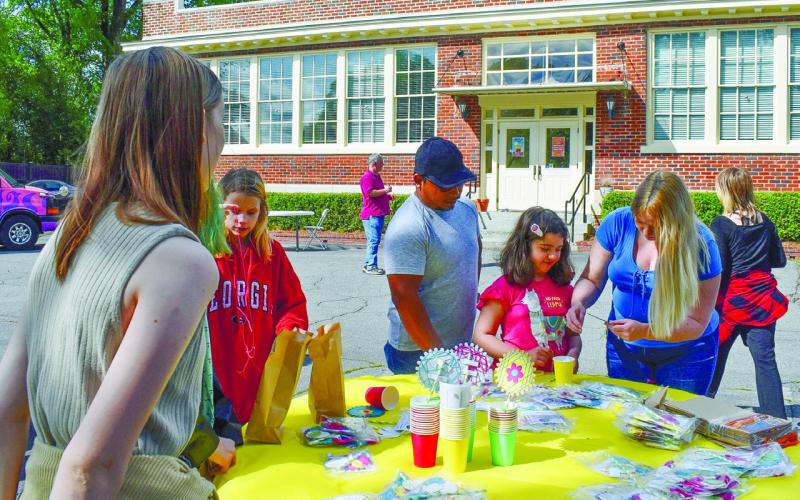 Katie Lopez helps her daughter Melanie Lopez to make a flower in a cup as Gerardo Lopez looks on, volunteer Madison Martin unravels a string, and volunteer Amy Moss watches the process.