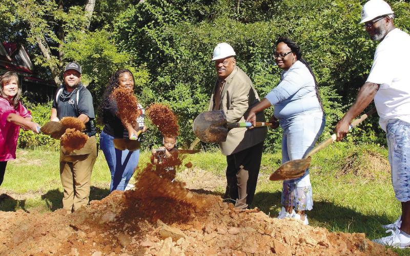 With tiny Journiee Burnney peering out from the center, her mother Ikeirra beside her was joined by (l-r) Habitat board member Linda Moore, builder Clark Harper, Eatonton Mayor John Reid and other family members as they each tossed a ceremonial shovelful of dirt for the World Habitat Day groundbreaking.