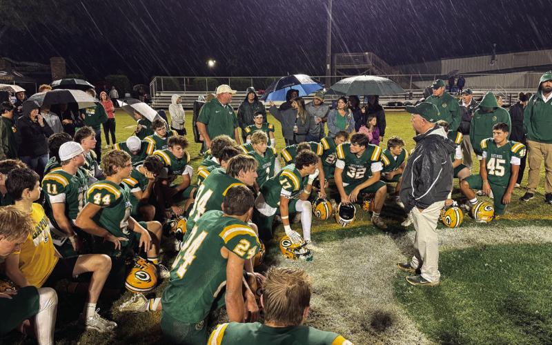 With steady rain falling, Gatewood head coach Jeff Ratliff (right, black jacket) addresses his team at midfield after a disappointing 30-17 loss last Friday to the visiting Windsor Academy Knights, from Macon.