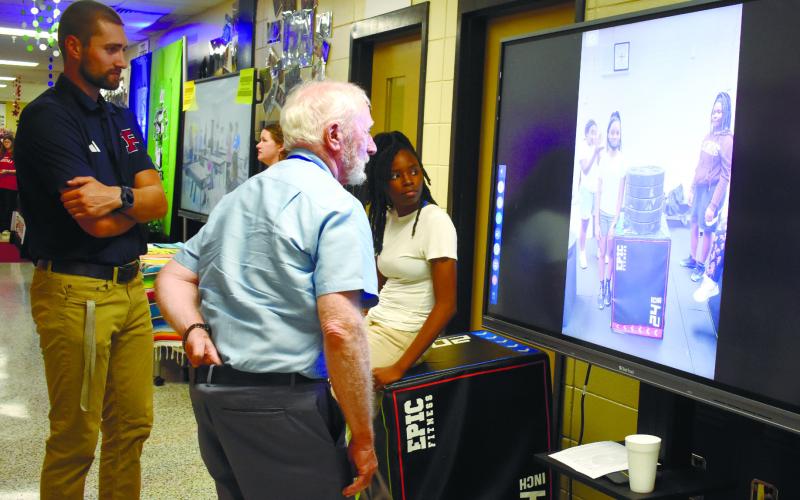 Coach Beau Beasley and student athlete Aiyana Crawford show Board of Education Chairman Dr. Steve Weiner videos of the weight training class.