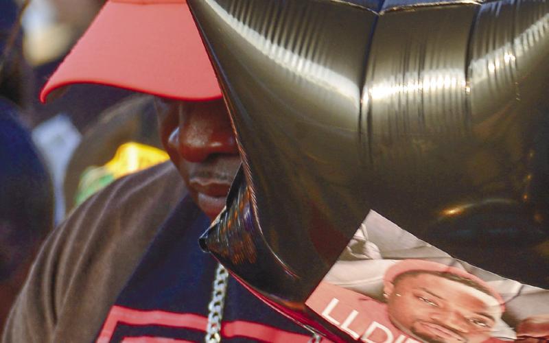 Frederick Scott Sr. bows his head in prayer Friday night while holding a memorial balloon with his son Frederick Jr.’s image printed on it.