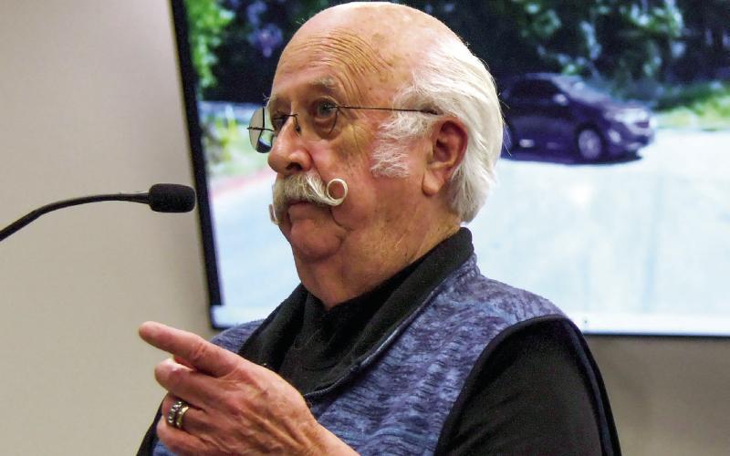With a video of the intersection of Twin Bridges and Dennis Station Roads playing on screens behind him, past county chairman Billy Webster addressed the current Putnam County Commission about the intersection’s safety issues. IAN TOCHER/Staff