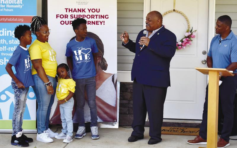 Eatonton Mayor John Reid hands over the keys to a brand-new Habitat home to Cerria and her three kids while former NFL star Warrick Dunn enjoys the moment.