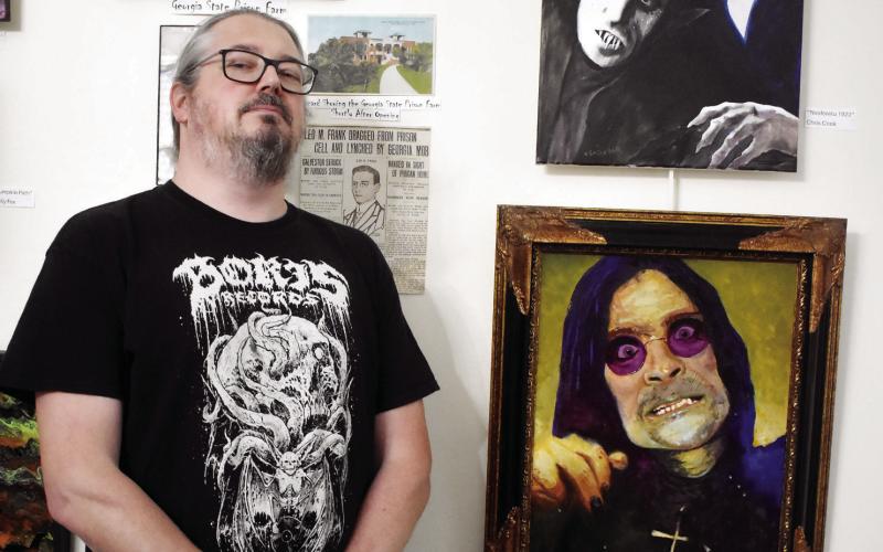 Artist Chad Wilson poses with his piece “Sabbath Bloody Sabbath” (bottom right) at The Marlor House. BAILEY BALLARD/Staff