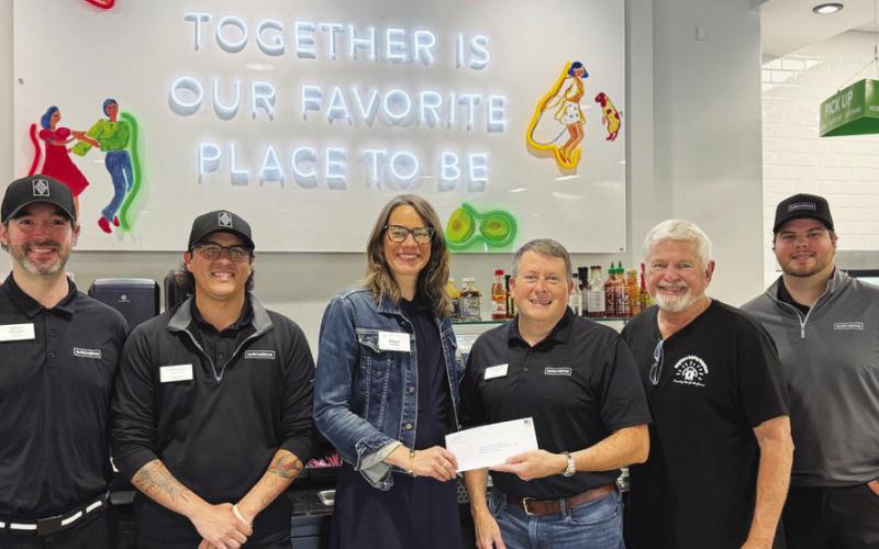 Neighbors Helping Neighbors Executive Director Allyn Rippin (center) accepts a donation from Surcheros owner Kyle Cullars, with several Surcheros employees standing by in support. CONTRIBUTED